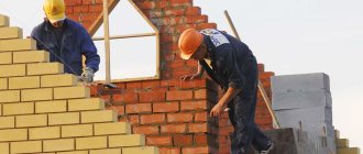 Рабочие выкладывают стену дома из кирпича